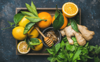A wooden tray with oranges, lemons, ginger, basil, and a bowl of honey with a honey dipper.