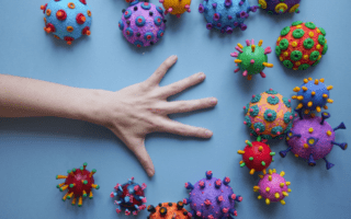 A hand reaches towards colorful, toy-like virus models on a blue background. A hand reaches towards colorful, toy-like virus models on a blue background.